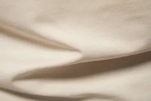 Close-up detail of soft beige cotton fabric showing natural texture and smooth folds.