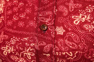 Close-up detail of men's red paisley printed long sleeve shirt with brown button placket.