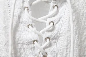 Close-up detail of a white lace-up V-neck shirt featuring metal eyelets and textured fabric.
