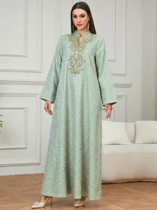Detalle de vestido largo verde elegante con manga larga, bordado dorado y patrón étnico.
