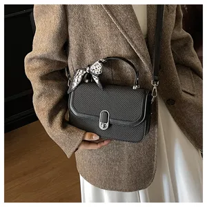 Detail shot of women black textured shoulder bag with metal lock and stylish handle scarf accessory