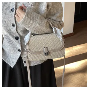 Detail shot of beige woven crossbody bag with silk scarf and metal lock in indoor setting.