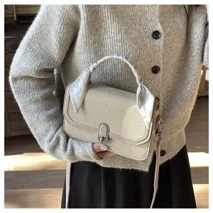 Woven crossbody bag detail showing elegant handle scarf and metal lock closure design.
