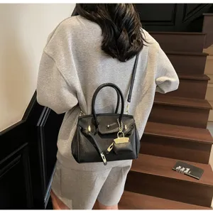 Vue détaillée d'un sac à main en cuir noir avec poignées, détails dorés et cadenas chic.