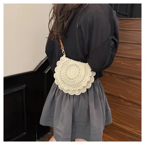 Detalle del bolso cruzado de paja tejida que muestra la forma de concha y la correa fina.
