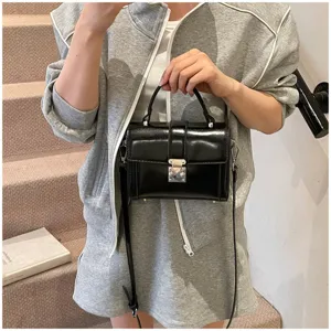 Close-up detail of stylish black patent leather mini box bag with metal lock and handle.