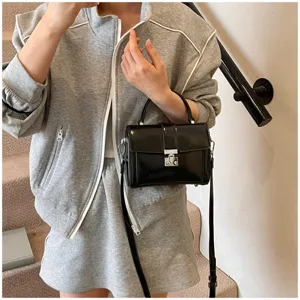 Close-up view of a stylish black glossy box handbag showcasing the metallic lock and strap.