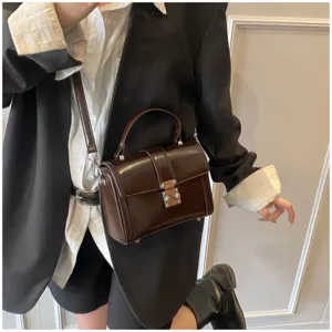 Detailed view of dark brown structured box bag with metal lock, stylish shoulder strap and handle.