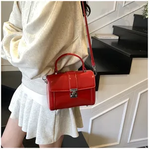 Detailed view of the red patent leather shoulder bag with top handle and metal lock.
