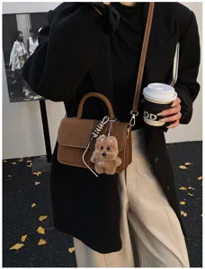 Detailed view of trendy brown shoulder handbag featuring cute plush puppy charm and hardware.
