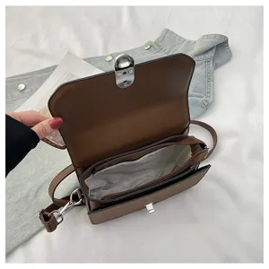 Detail view of brown leather crossbody bag with multi-compartment interior and metal lock.