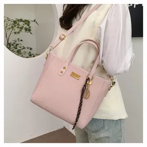 Pink woven texture shoulder bag detail, elegant dual top handles and metal charm decoration.
