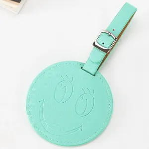 Étiquette de bagage ronde en cuir PU vert menthe avec visage souriant et boucle métallique.