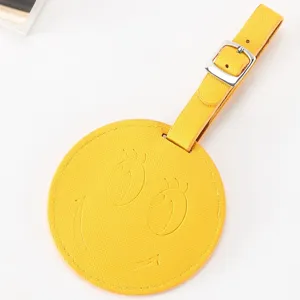 Étiquette de bagage ronde en cuir PU jaune avec visage souriant gaufré et boucle métallique.