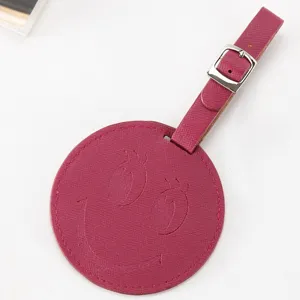 Étiquette de bagage ronde en cuir PU avec visage souriant gaufré et sangle à boucle réglable.