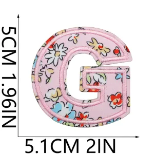 Vista di dettaglio della lettera G ricamata con fiori rosa, stemma decorativo per vestiti e borse.