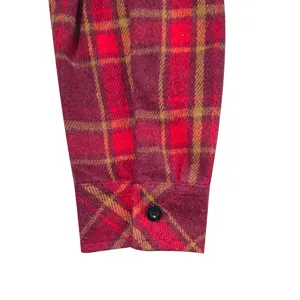 Close-up detail of red and yellow plaid flannel shirt sleeve cuff with black button.