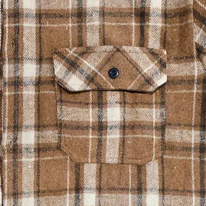 Close-up detail of men's brown plaid flannel shirt pocket showing vintage check pattern and button.