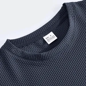 Nahaufnahme des dunkelgrauen Textur-T-Shirt-Kragens mit Stoffdetail und dem Etikett.