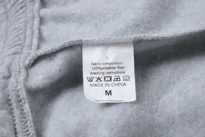 Dettaglio etichetta di cura jogger in pile grigio, 100% fibra di poliestere, taglia M, dettaglio.