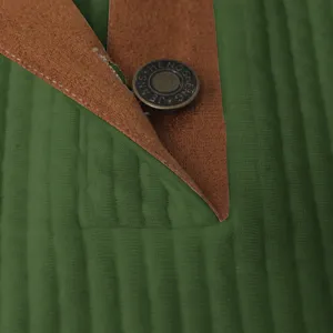 Close-up detail of men's green textured jacket with metallic snap button and brown leather trim.