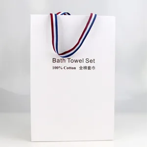 Detailed view of white paper gift bag for bath towel set with striped ribbon handles.