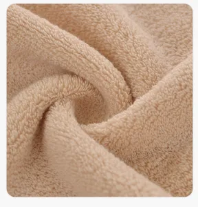 Close-up of soft beige cotton towel fabric, showing fine terry cloth texture and plush feel.