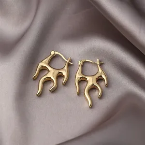 Nahaufnahme goldener Flammenohrringe im minimalistischen Punk-Stil auf Seidenstoff