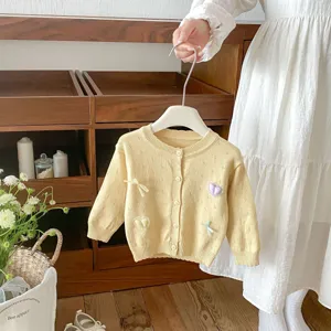 Close-up detail of infant yellow knitted cardigan featuring cute heart embroidery and bows.