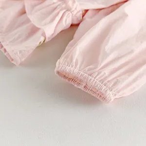 Détail manche cardigan rose bébé, haut léger pour nourrisson avec volants et poignets élastiques.