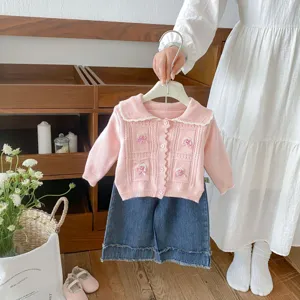 Detail view of pink knit cardigan with sweet bow embroidery and denim shorts in warm indoor scene.