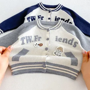 Détail de cardigan tricoté pour enfants, broderie de lettres et couleur contrastée.