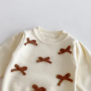Dettaglio maglione in maglia neonata, fiocchi marroni carini, top girocollo morbido.