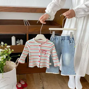 Close-up detail of baby girl striped knit cardigan and denim pants set with cute bows.