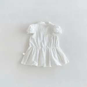 Vue détaillée d'une robe blanche à manches courtes pour bébé fille brodée de motifs ajourés.