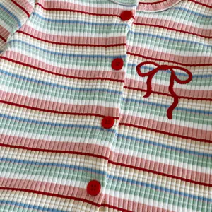 Close-up detail shot of baby girl knitted striped cardigan with red buttons and bow embroidery.