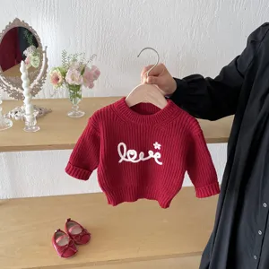 Detailed view of girls red knit sweater featuring white letter embroidery and cozy texture.