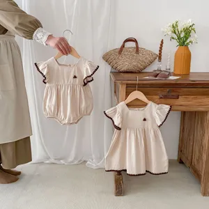 Detailed shot of cute baby girl romper and dress set in light beige with brown trim.