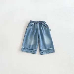 Close-up detail of cute kids denim wide-leg pants showing heart embroidery and raw frayed hems.