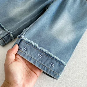 Close-up detail of girls light blue denim jeans with cute white heart embroidery and raw hem.