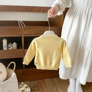Infant yellow knitted cardigan detail shot, soft baby sweater texture on wooden shelf background.