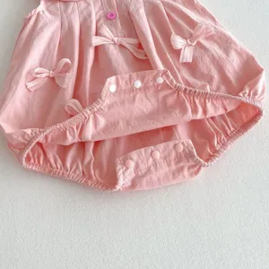 Primer plano detallado de un tierno pelele rosado para bebé con lazos decorativos y broches.