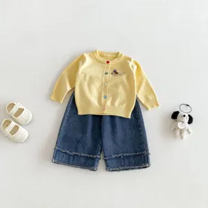 Detail shot of infant yellow knit cardigan with dachshund embroidery and blue denim pants.