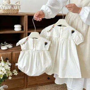 Vista dettagliata del grazioso set tutina e abito in cotone per neonata con ricamo.
