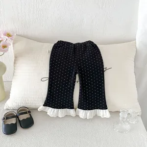 Detailed shot of toddler girl black polka dot flare pants with white lace trim on cozy pillow.