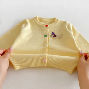 Infant yellow knit cardigan detail, cute dachshund embroidery and colorful buttons closeup view.