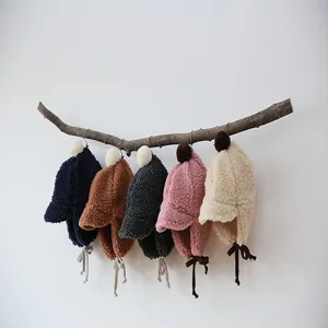Detailed view of cute plush infant earflap hats in assorted colors hanging on a natural branch.