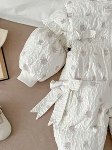 Infant winter down jumpsuit detail, white ruffled design with pink floral pattern and bow.