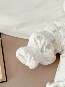 Infant winter jumpsuit sleeve detail, white quilted fabric with cute bow pattern, soft cuff.