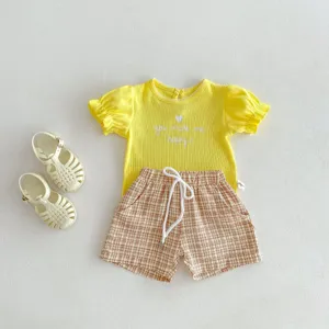 Vue de détail d'un t-shirt bébé jaune avec lettres et short à carreaux pour enfants.